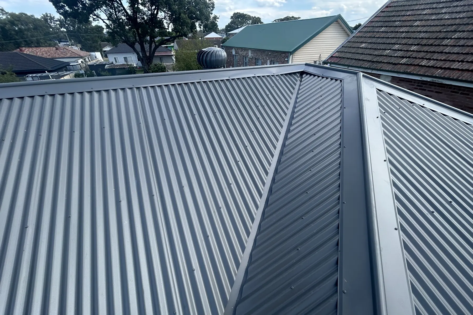 New charcoal corrugated steel sheeting along the hip of a re-roofed house, tiled neighbouring roofs behind